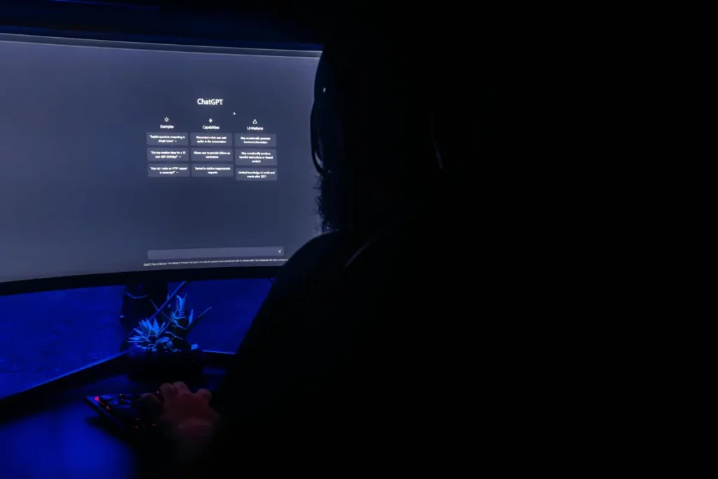 Person working on a computer in a dark room with the ChatGPT interface displayed on a curved monitor, showcasing AI capabilities.