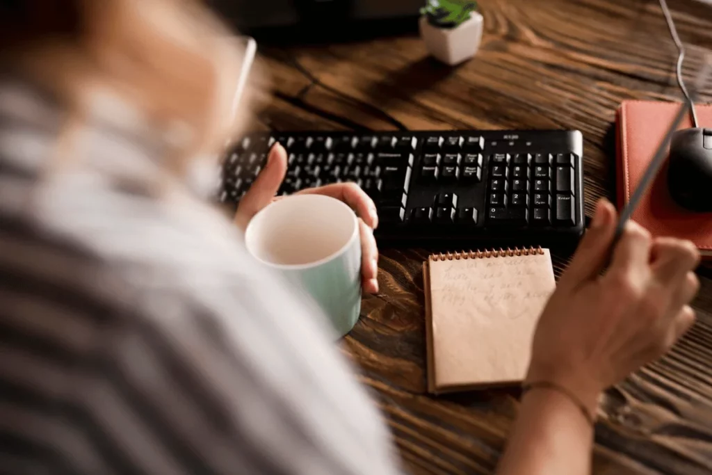 A person is sitting at a desk with a cup of coffee and a notebook.