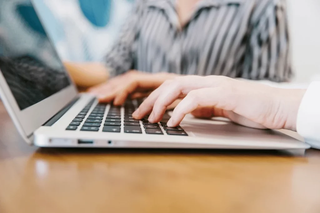 A person typing on a laptop computer, focused on the screen, with a cup of coffee beside them.