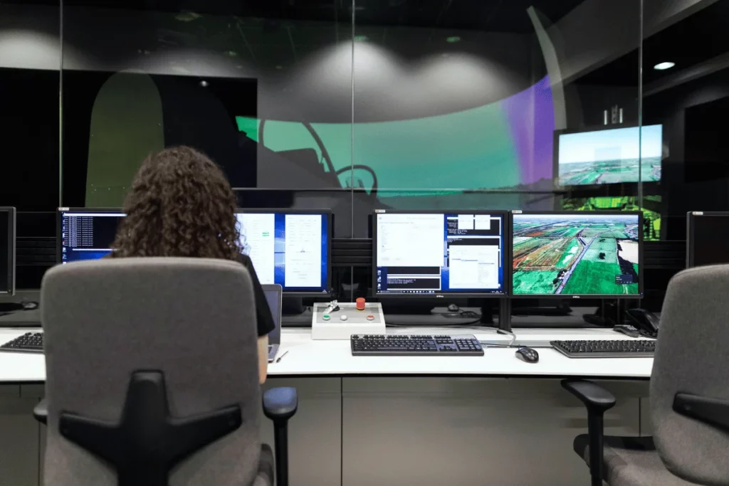 A person with curly hair sitting at a control center with multiple monitors.