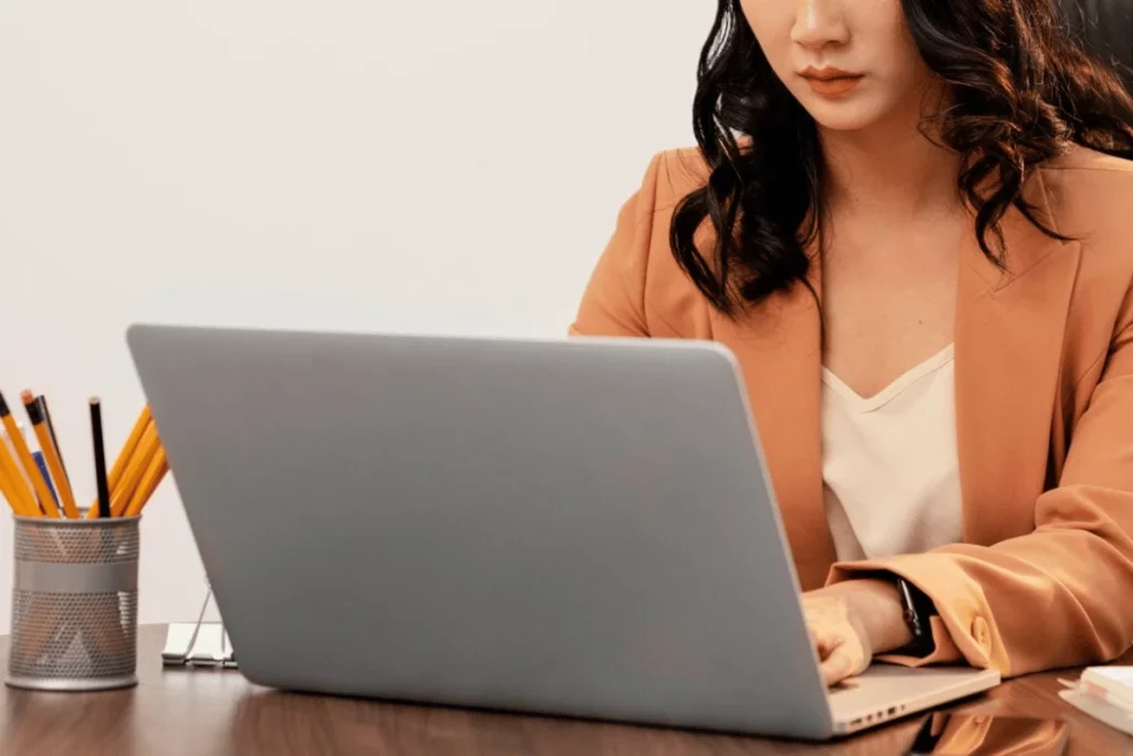 A person in a brown blazer sitting at a desk with a laptop.