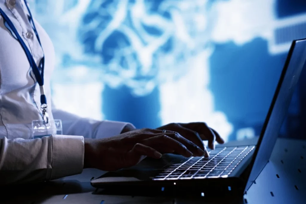 A person typing on a laptop computer in front of an image of a brain.