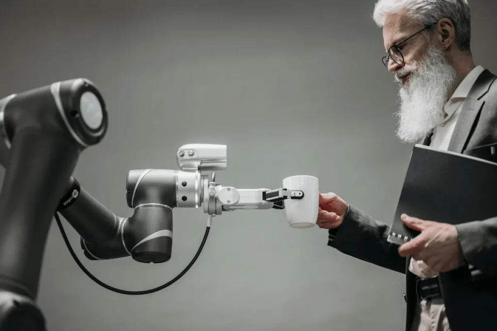 Bearded man interacting with a robotic arm holding a cup, showcasing advanced robotics and human-technology collaboration.