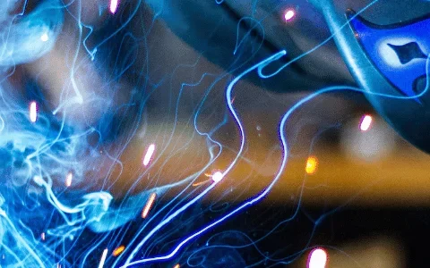 Close-up of a welder in action with bright blue sparks flying from the welding torch.