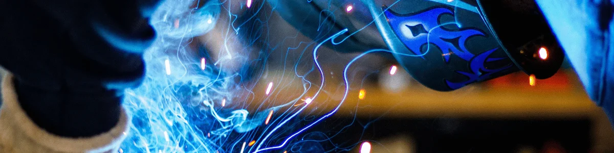 Close-up of a welder in action with bright blue sparks flying from the welding torch.