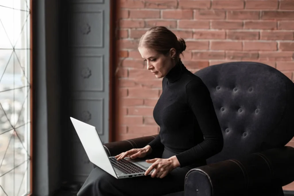 A person sitting on a chair with a laptop in front of a brick wall.