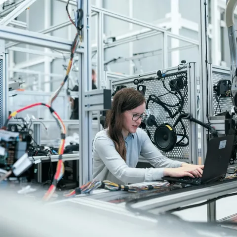 A woman working on a laptop in a high-tech laboratory filled with intricate machinery.