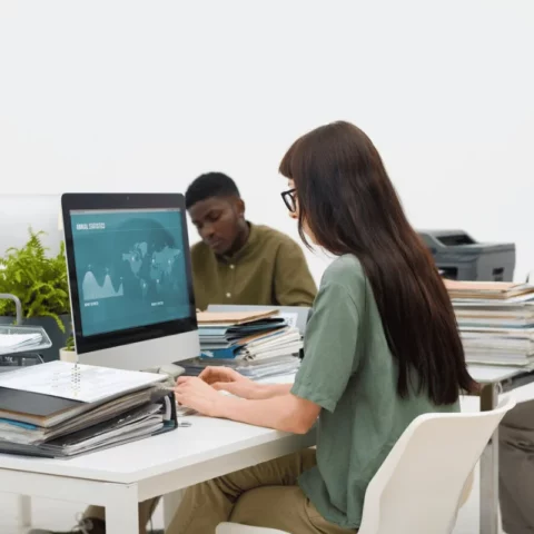 Office workers concentrating on their tasks, with one using a desktop computer showing annual statistics.