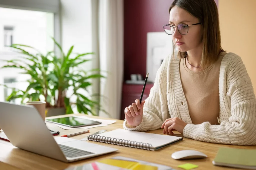 A person in glasses sitting at a desk with a laptop.