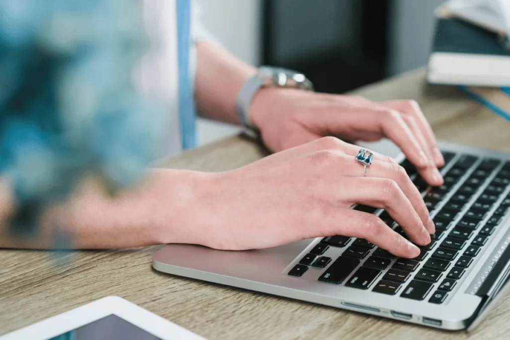 Close-up of hands working on a laptop keyboard in an office setting.