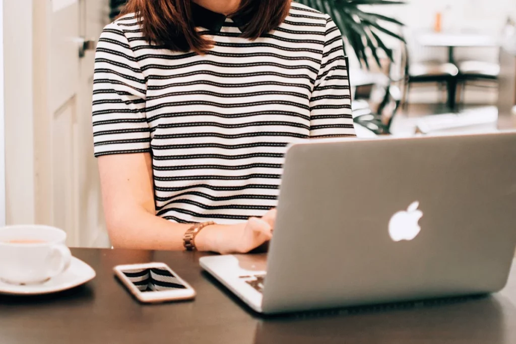 Woman in a striped shirt working on a laptop at a desk with a coffee cup and smartphone.