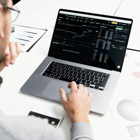 Man analyzing cryptocurrency data on a laptop, with charts and graphs spread on the desk.