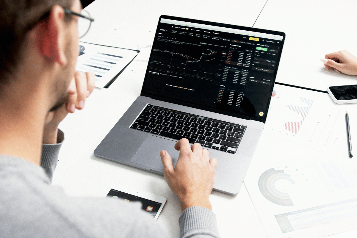 Man analyzing cryptocurrency data on a laptop, with charts and graphs spread on the desk.