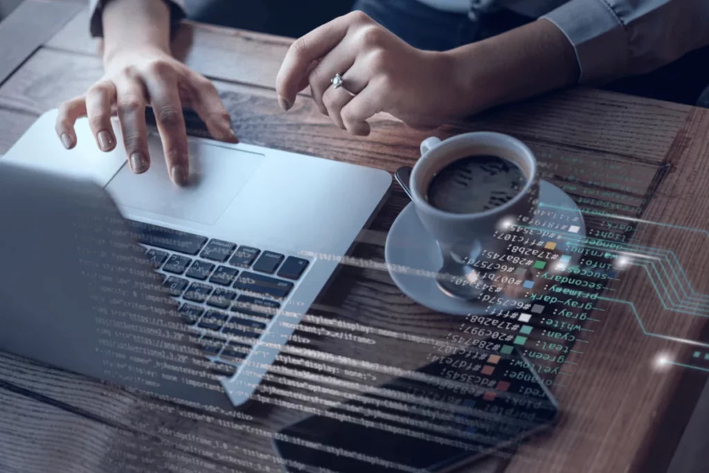 Laptop keyboard being used with coding lines overlayed and a coffee cup on the desk.