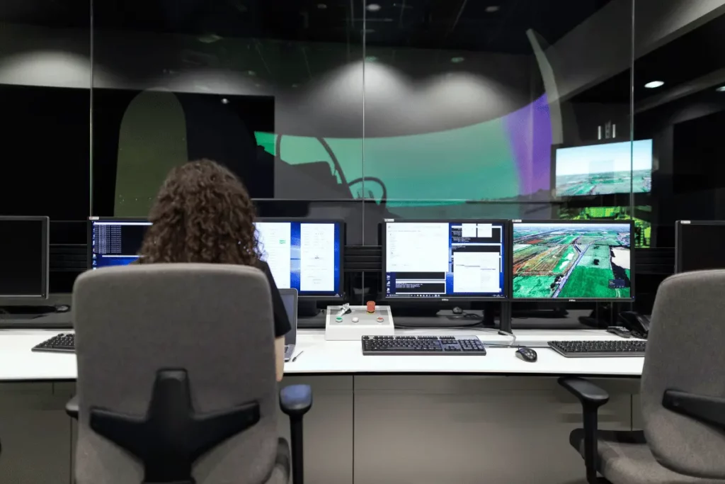 Back view of a technician at a multi-screen workstation in a control room.