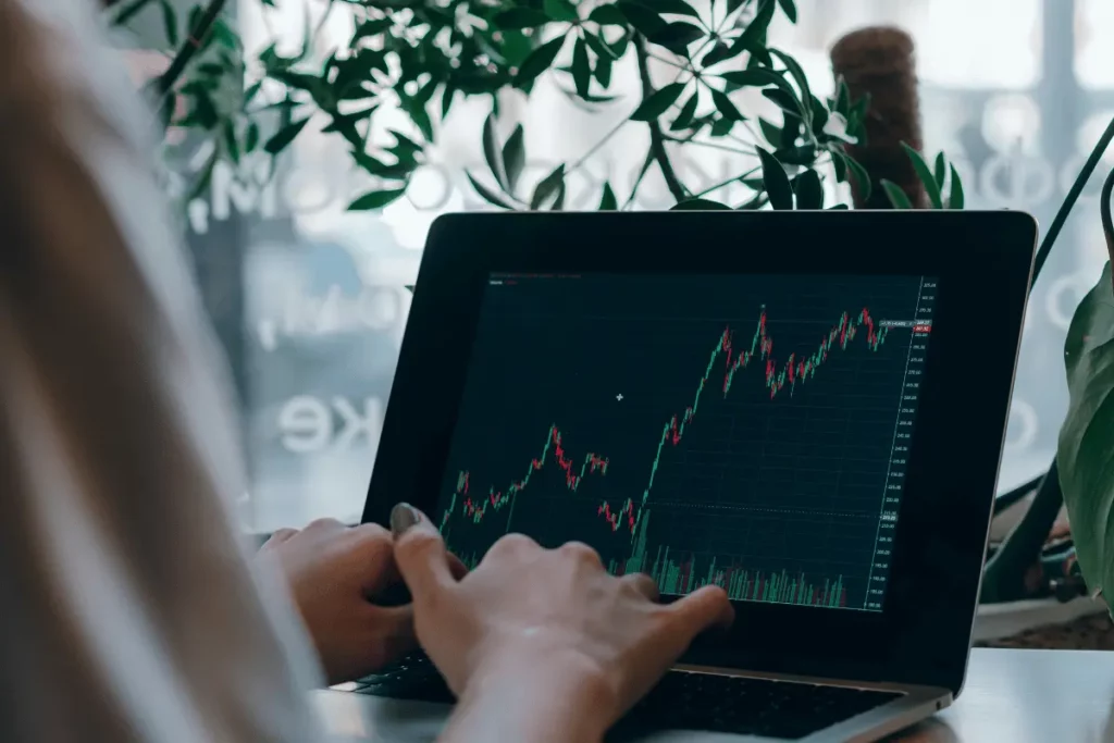 Person analyzing stock market graph on a laptop screen with green plants in the background.