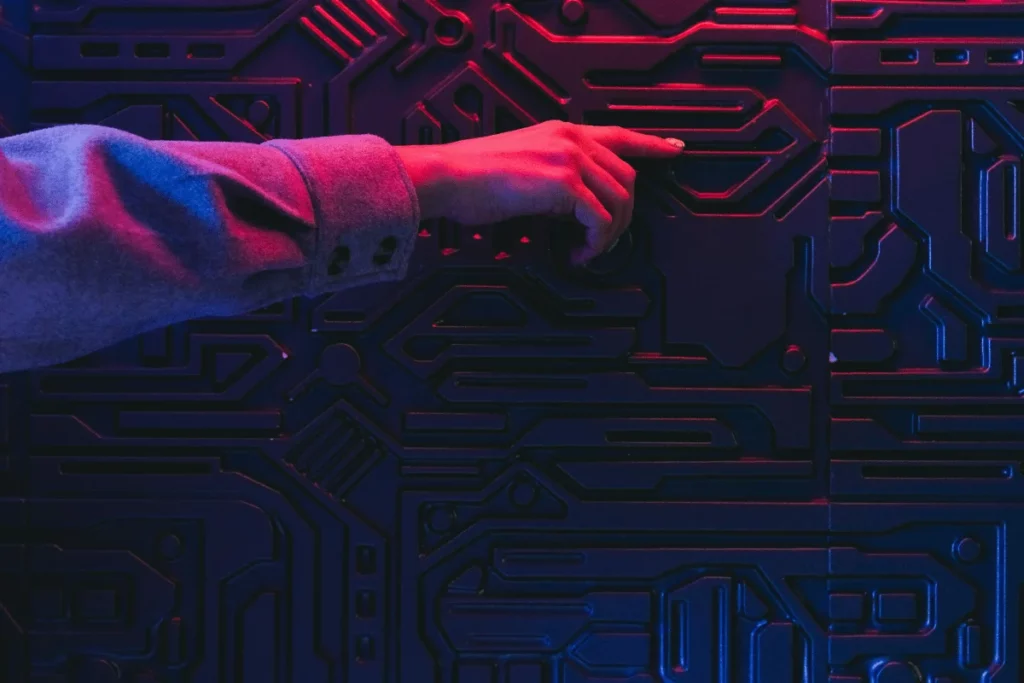 Person's finger touching a neon-lit circuit patterned wall in dark ambiance.