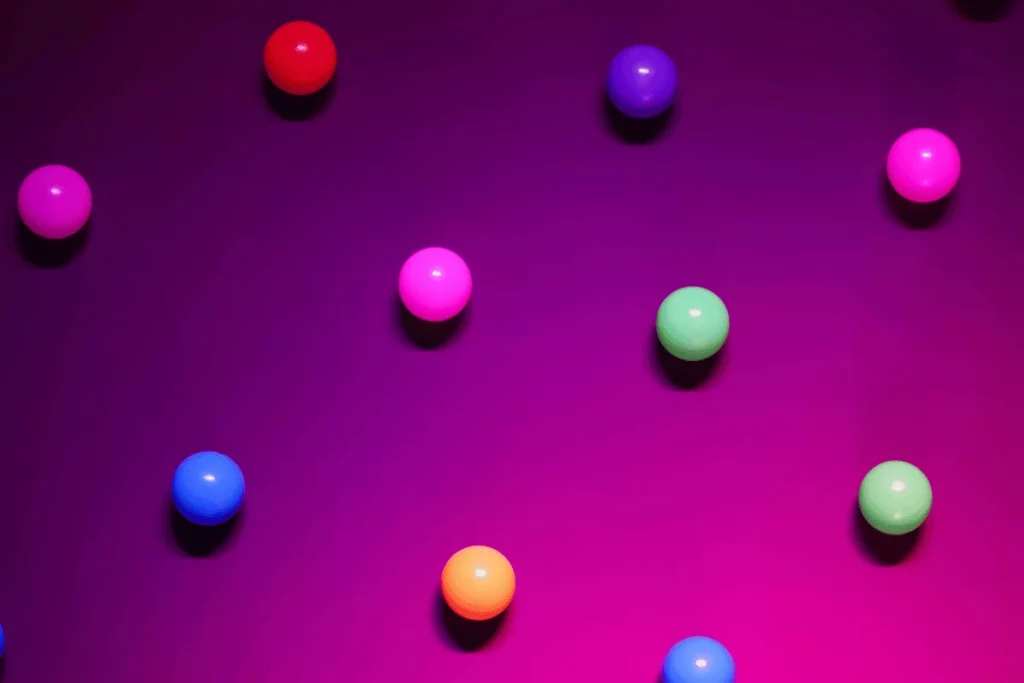 A series of brightly colored balls in red, pink, green, blue, and orange, floating against a purple backdrop.