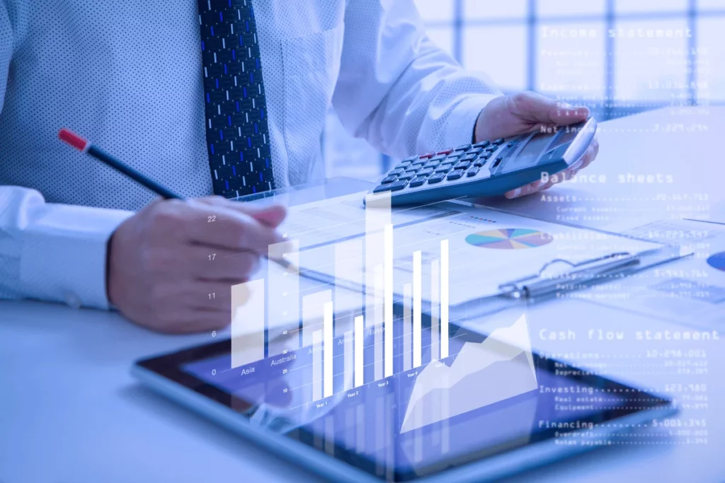 Person analyzing financial data with calculator on digital tablet overlaying graphs.