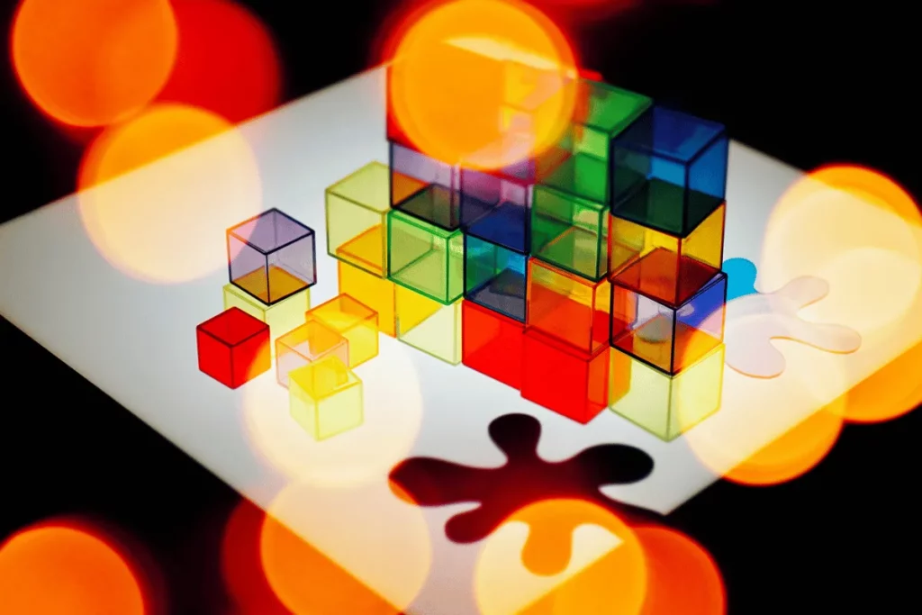 Colorful translucent cubes on a glossy surface with soft bokeh lights in the background.