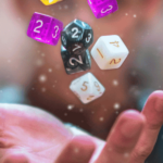 Open hand with floating colorful polyhedral dice, sparkles around, blurred background.