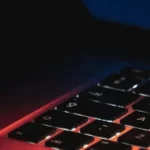 Backlit laptop keyboard with colorful screen glow in a dark setting.