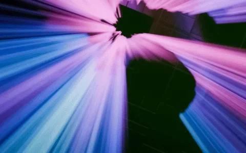 Abstract light beams in vibrant shades of blue and pink radiate from a central point against a dark background, creating a dynamic visual effect.