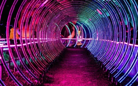 A brightly lit neon tunnel with swirling purple and blue lights, featuring a child in a red shirt walking through it.