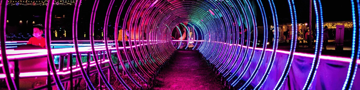 A brightly lit neon tunnel with swirling purple and blue lights, featuring a child in a red shirt walking through it.