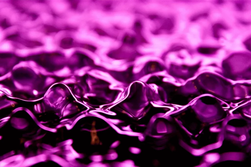 Abstract close-up of fluid purple waves, with shimmering reflections creating a smooth, rippling surface effect.