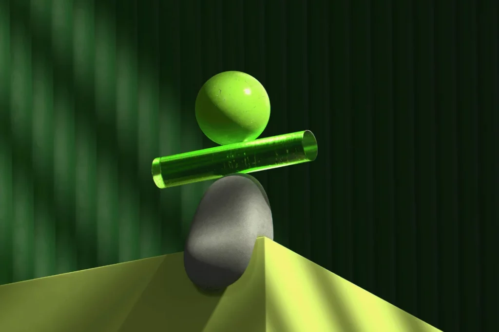 A green sphere balanced on a transparent green cylinder, resting on a gray rock on a yellow surface.
