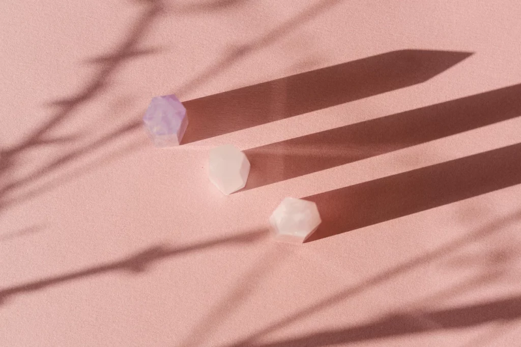 Minimalist crystal shapes on pastel pink background.